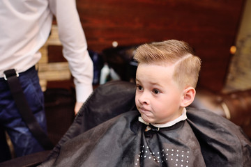 little baby boy in a barber's chair looks at his haircut in the mirror