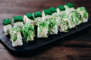 Sushi rolls set on black wooden tray, close up. Asian restaurant menu, food  photo art. Traditional Japanese cuisine.