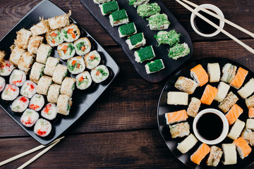 Delicious fresh appetizing sushi set on black plates, flat lay. Traditional japanese food, restaurant serving