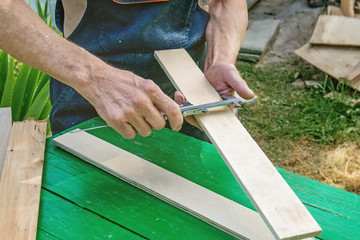 The master sharpens the wooden panel with an electric grinder on a Sunny day in the garden. Dimensioning