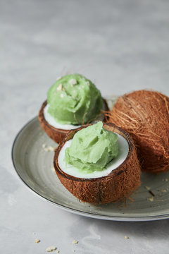 Tasty fresh green fruit ice cream in coconut peel with whole fresh coconut on gray background.