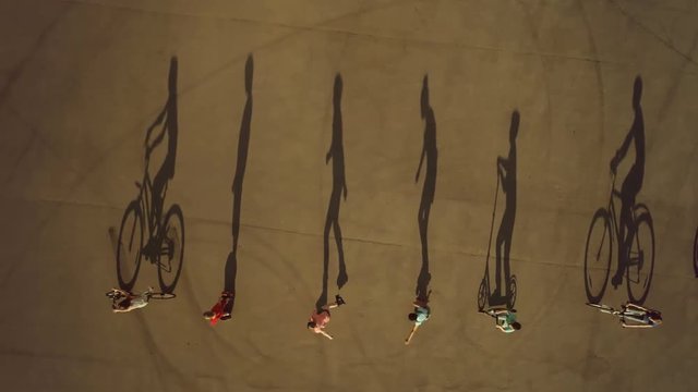 Children riding in row on bikes, roller skates and scooters cast long shadows. Top view