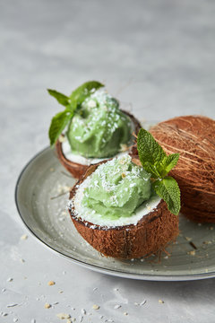 Fresh green mint ice cream in coconut shell with whole fresh coconut on a plate on a gray concrete.