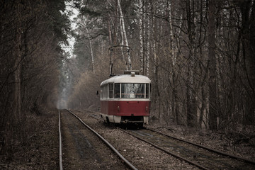 Obraz premium Vintage red tram running through the forest part of the city. Autumn background in the park in Kiev, Ukraine.