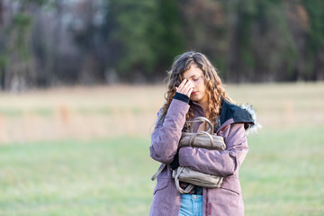 Young unhappy woman girl walking with head eyes closed down holding hugging purse in winter coat,...