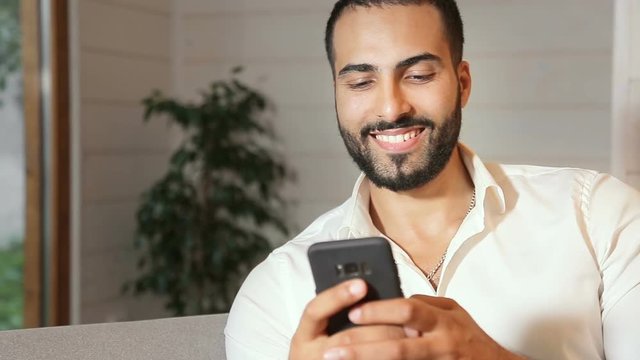 Asian young man in prisine white shirt texting a message on black smartphone, using technology as having day off at home