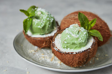 Delicious homemade green ice cream in a coconut shell, mint leaf with whole coconut on a gray background.