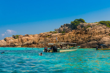 Tourists are snorkelling in crystal clear turquoise blue water at the popular Tokong Burung (Bird Island) site, an island made up mostly of towering boulder rocks near Perhentian Kecil, Malaysia.