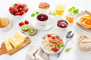 healthy breakfast with oatmeal porridge, strawberry, nuts, toast, jam and tea