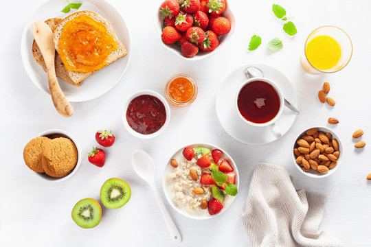 healthy breakfast with oatmeal porridge, strawberry, nuts, toast, jam and tea. Top view