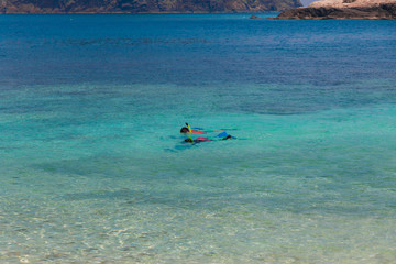 Fototapeta na wymiar Two tourists snorkelling in the turquoise blue sea, in front of the shallow clear waters of Rawa beach, an island near Perhentian Kecil in Malaysia.