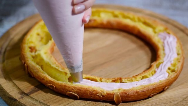 Half of a Paris Brest cake. Background: a pastry bag filling with whipped cream.