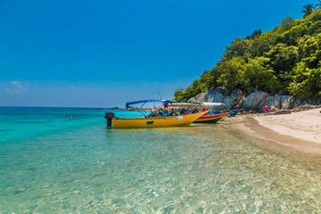 Colourful tourist boats anchored on the glimmering shallow water of Rawa beach; its white powdery sand, lush forest and big rocks in the background and the blue sky makes this a great holiday scene.