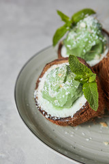 Close-up of delicious green ice cream with mint leaf in a coconut shell on a gray plate.