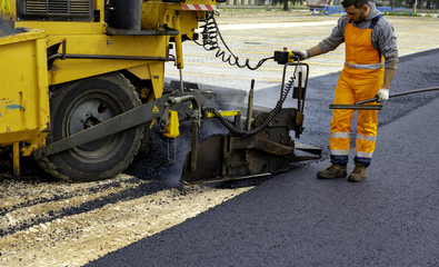 Workers regulate tracked paver laying asphalt heated to temperatures above 160 ° pavement on a...