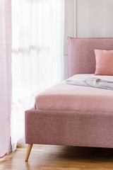 Dirty pink, comfy bed by a window with sheer curtains in a bright bedroom interior