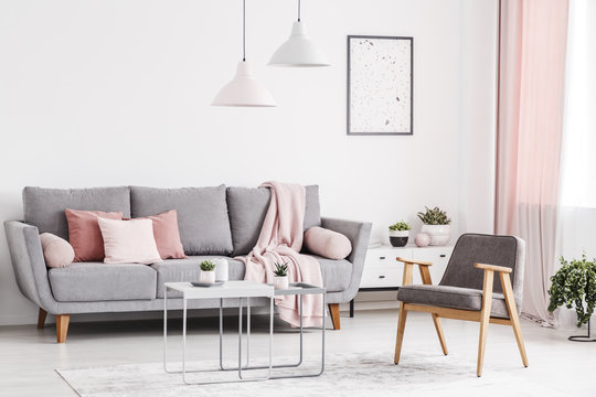 Retro armchair, grey sofa with pink pillows and coffee tables in an elegant living room interior. Real photo