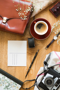 Top view on wooden desk with camera and cup of coffee next to red bag and postcard