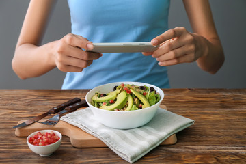 Woman taking photo of healthy salad with mobile phone