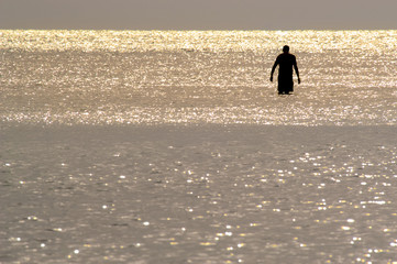 Silhouette of a solitary man wading in shiny water at sunset on Barefoot Beach, Florida