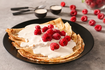 Plate with tasty thin pancakes and berries on light table