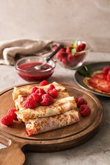 Board with tasty thin pancakes and berries on light table