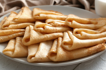 Plate with tasty thin pancakes on table, closeup