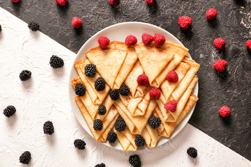 Plate with tasty thin pancakes and berries on table