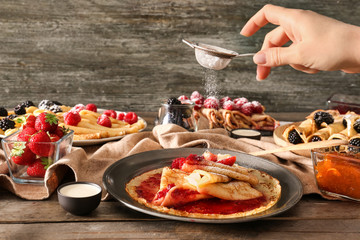 Woman sprinkling tasty thin pancakes with sugar powder at wooden table