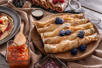 Plate with tasty thin pancakes, berries and jam on wooden table