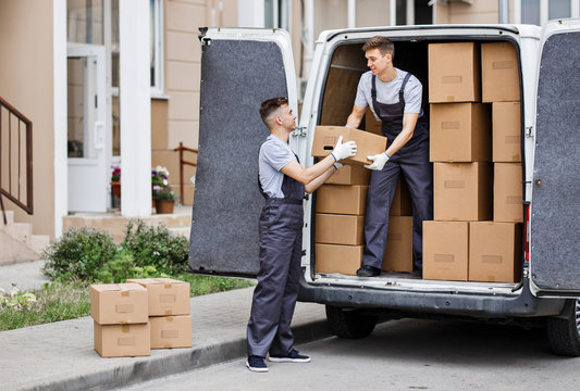 Two young handsome movers wearing uniforms are unloading the van