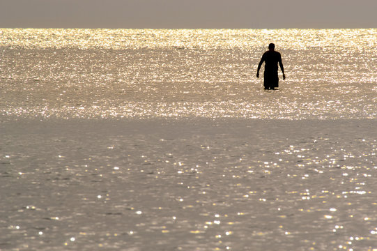 Silhouette of a solitary man wading in shiny water at sunset on Barefoot Beach, Florida - Powered by Adobe