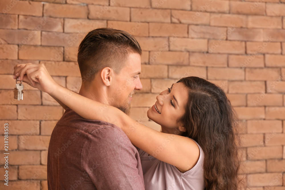 Wall mural happy young couple with key from their new house near brick wall