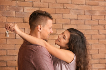 Happy young couple with key from their new house near brick wall