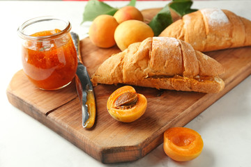 Jar with delicious apricot jam and  croissants on wooden board