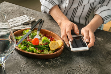 Woman with mobile phone and healthy fresh salad on plate