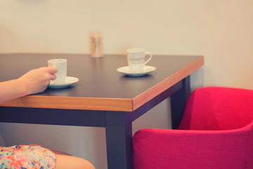 A girl hand with a cup of coffee for espresso on an armchair in a cafe