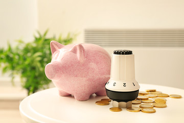 Thermostat, piggy bank and coins on table at home. Heating saving concept