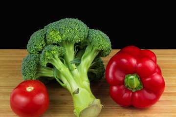 Red pepper, tomato and broccoli on wooden table