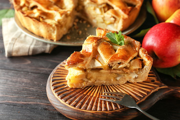 Board with piece of delicious apple pie on wooden table, closeup