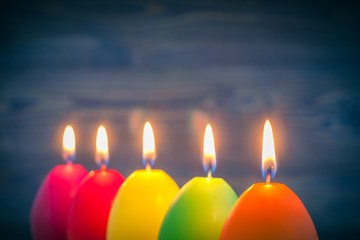 A row of colored candles burn on a wooden background