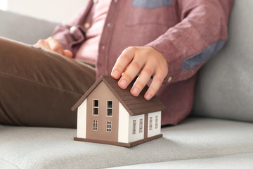 Man with house model sitting on sofa, closeup. Mortgage concept