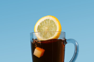 A fresh juicy yellow lemon with a sugar cube flies into a cup of Ceylon black tea on a blue background.