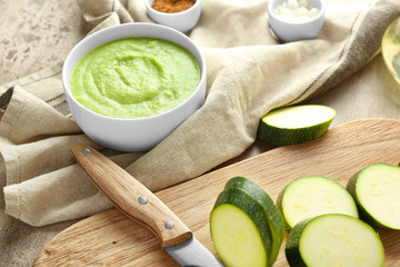 Tasty zucchini soup in bowl with fresh sliced marrow on table