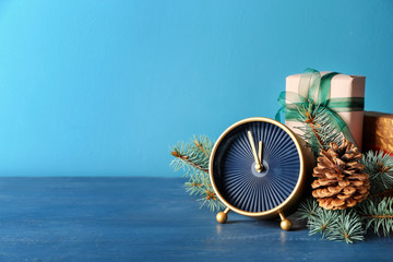 Alarm clock with gifts and fir branches on color background. Christmas countdown