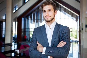 Portrait of happy businessman with arms crossed standing in office.