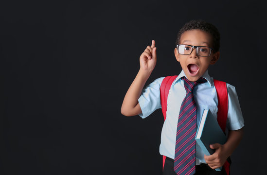 Cute African-American schoolboy with raised index finger on dark background