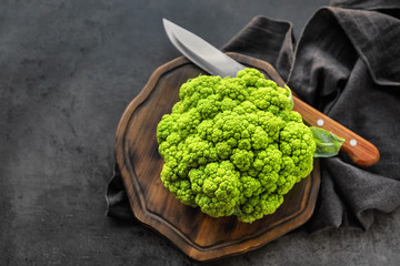 Green cauliflower with knife on wooden board