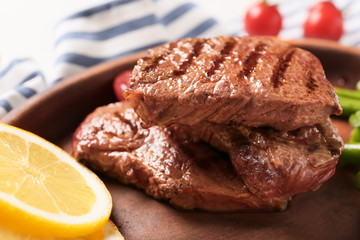 Tasty grilled steaks with sliced lemon on plate, closeup