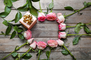 Frame made of beautiful roses and gift box on wooden table